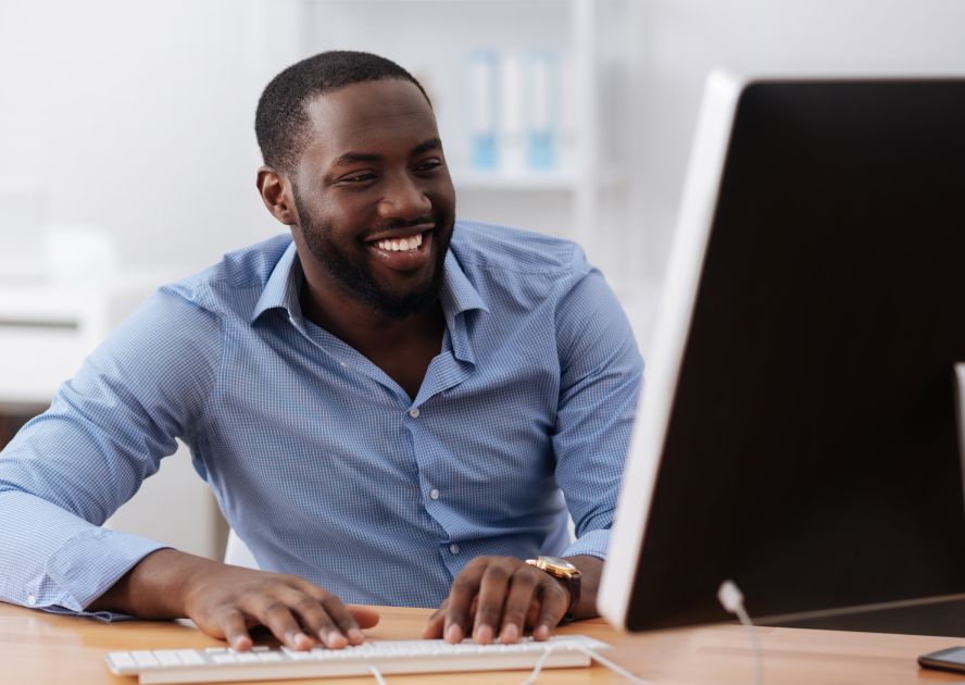 man in blue button down smiling at computer monitor